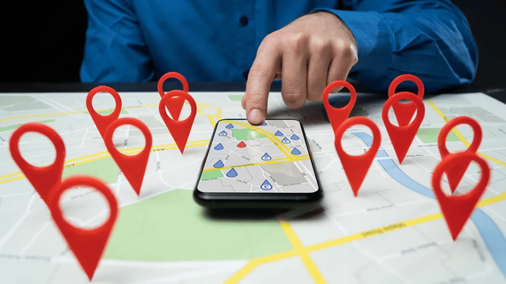 Hand using a smartphone with a map surrounded by red location pins.
