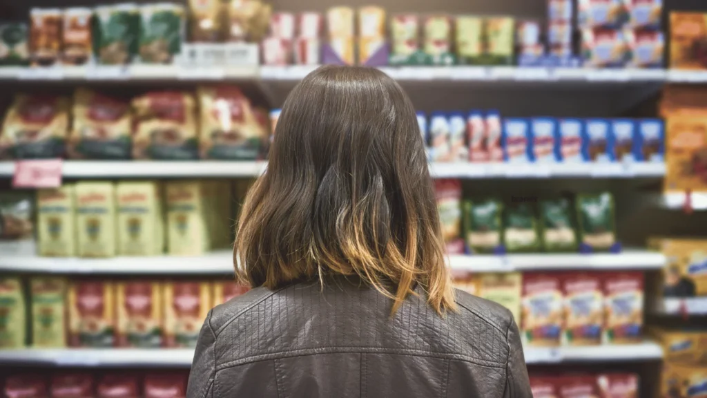 Rear view of a person looking at fully stocked grocery store shelves filled with various packaged products.